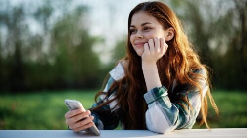 Young woman thinking about someone special and smiling at her phone